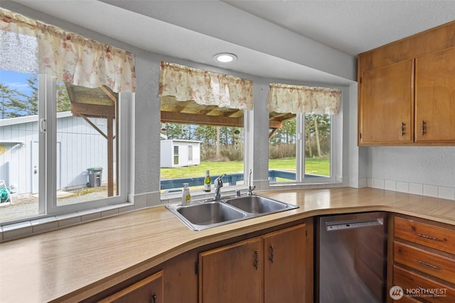 kitchen with dishwasher, light countertops, a textured wall, and a sink