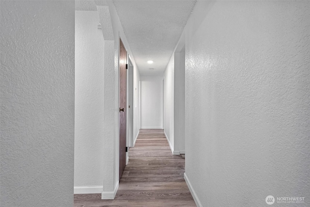 hall featuring a textured ceiling, wood finished floors, baseboards, and a textured wall