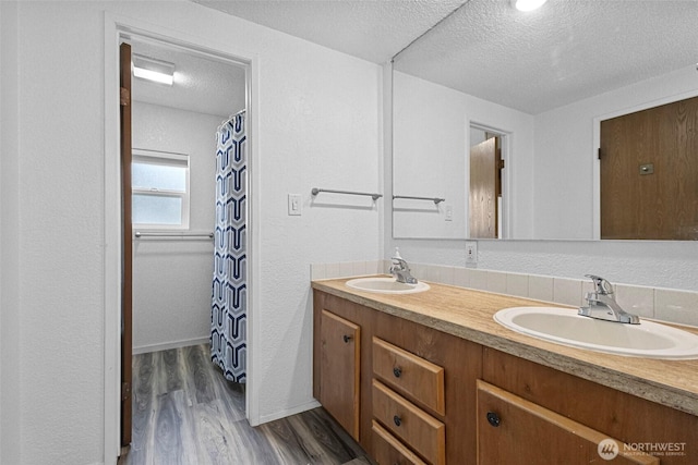 full bathroom with double vanity, wood finished floors, a textured ceiling, and a sink