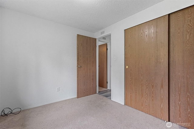 unfurnished bedroom featuring a closet, a textured ceiling, visible vents, and carpet flooring