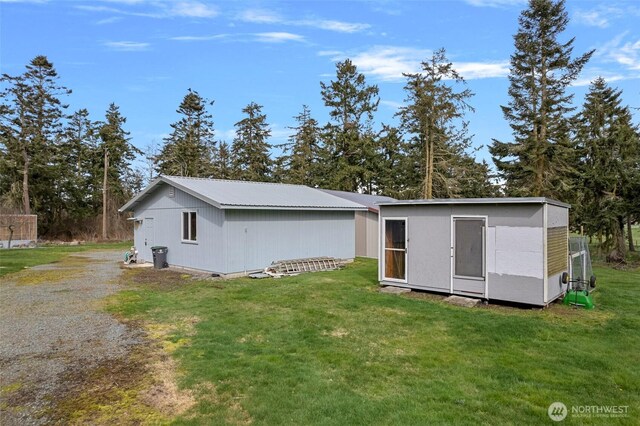 rear view of house featuring a lawn, driveway, metal roof, and an outdoor structure