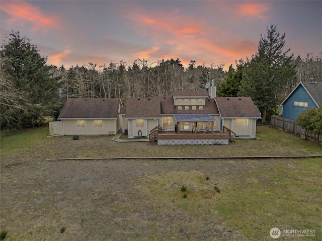 back of property at dusk with a wooden deck, a lawn, a chimney, and fence