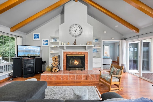 living area featuring built in shelves, beam ceiling, a tile fireplace, wood finished floors, and high vaulted ceiling