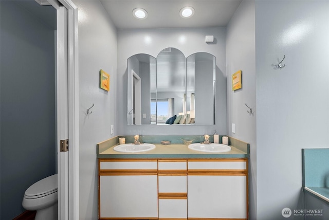 bathroom featuring a sink, toilet, recessed lighting, and double vanity