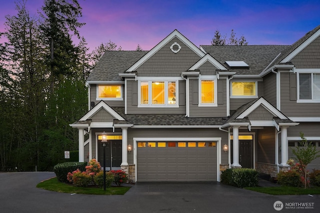view of front of property featuring stone siding, a shingled roof, driveway, and a garage