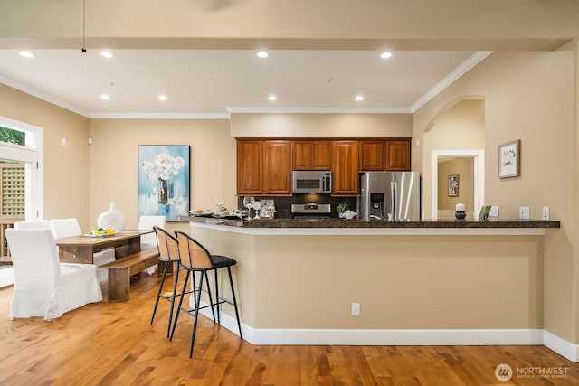 kitchen featuring stainless steel appliances, tasteful backsplash, crown molding, a kitchen bar, and brown cabinetry