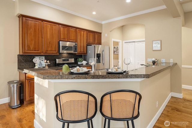 kitchen featuring light wood finished floors, dark countertops, a kitchen breakfast bar, and appliances with stainless steel finishes