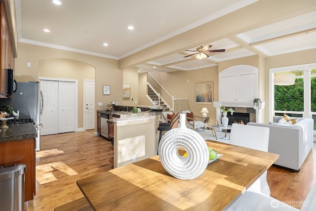 dining space featuring a warm lit fireplace, a ceiling fan, arched walkways, light wood-style floors, and stairs