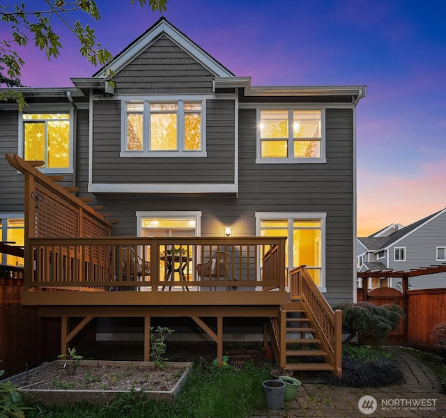 back of property at dusk with fence, a garden, a deck, and stairs
