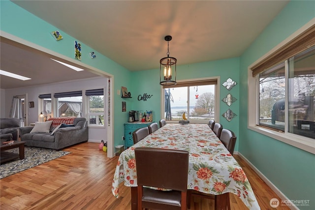 dining space featuring a notable chandelier, baseboards, light wood-style floors, and a skylight