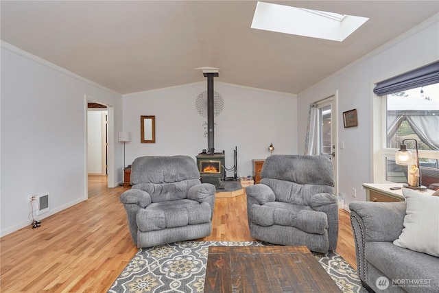 living area featuring visible vents, light wood-style flooring, a wood stove, and crown molding