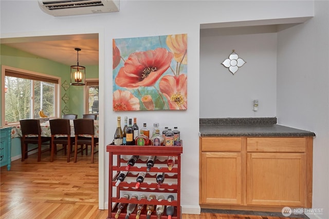 bar featuring light wood-type flooring, hanging light fixtures, and a wall unit AC