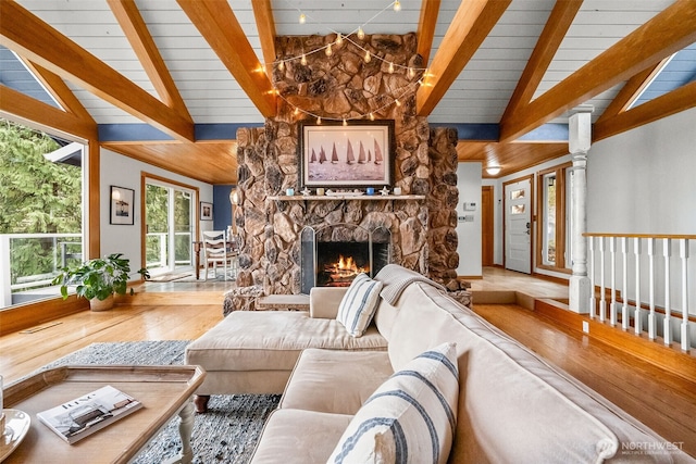 living area with a stone fireplace, wood finished floors, and vaulted ceiling with beams