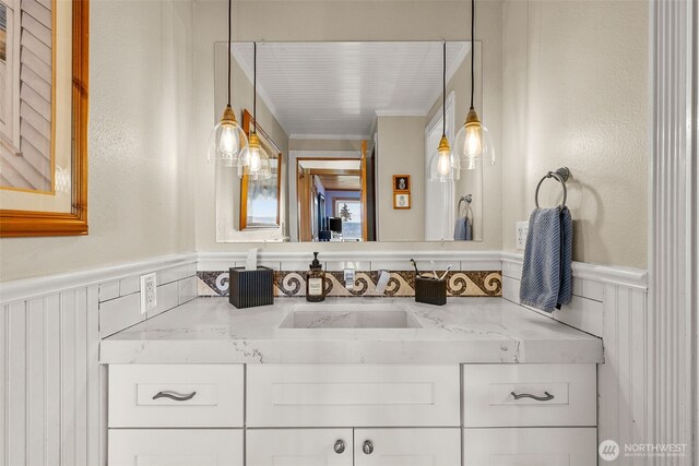 bathroom featuring a wainscoted wall, vanity, and ornamental molding