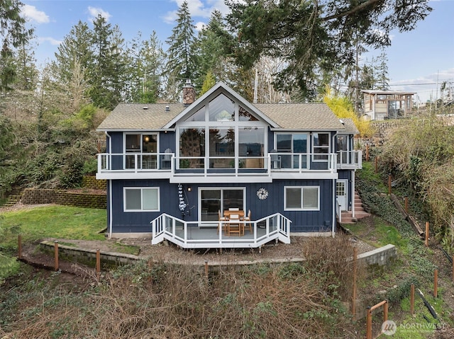 rear view of property featuring a chimney, roof with shingles, a sunroom, a wooden deck, and stairs