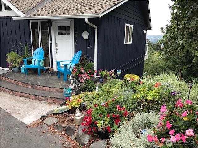 entrance to property with roof with shingles and a patio area