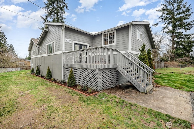 back of property with a wooden deck, a yard, and fence