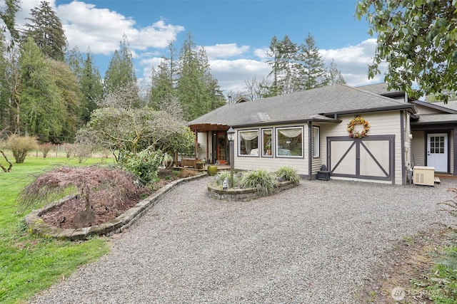 view of front facade with a garage, roof with shingles, and gravel driveway