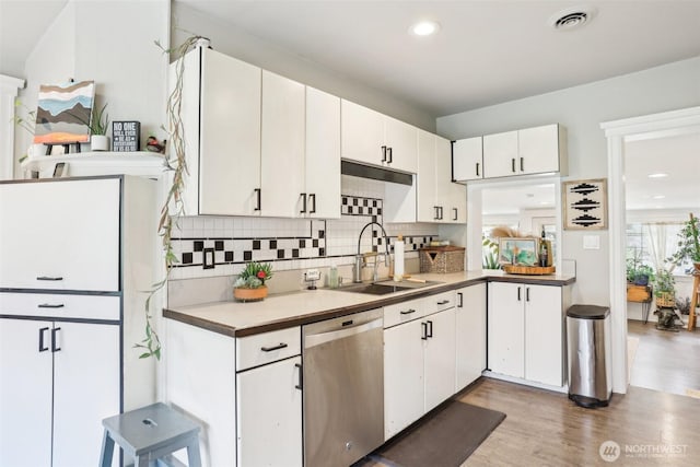 kitchen with a sink, decorative backsplash, white cabinets, light wood-style floors, and dishwasher