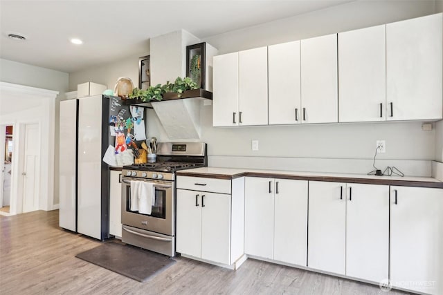 kitchen with visible vents, stainless steel range with gas cooktop, freestanding refrigerator, light wood-style floors, and white cabinetry