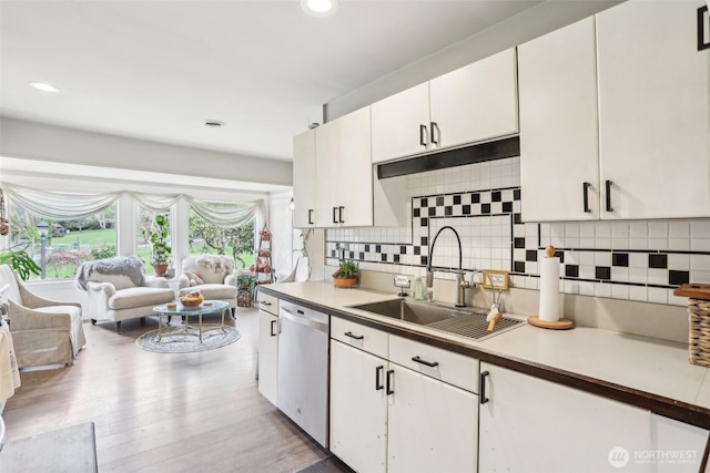 kitchen featuring light wood-style flooring, a sink, stainless steel dishwasher, backsplash, and white cabinets