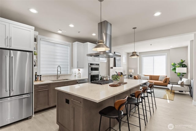 kitchen with a sink, a kitchen breakfast bar, a center island, appliances with stainless steel finishes, and island range hood