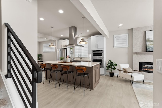 kitchen featuring white cabinetry, a fireplace, appliances with stainless steel finishes, a kitchen bar, and island range hood