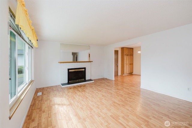 unfurnished living room with a brick fireplace, baseboards, and light wood finished floors