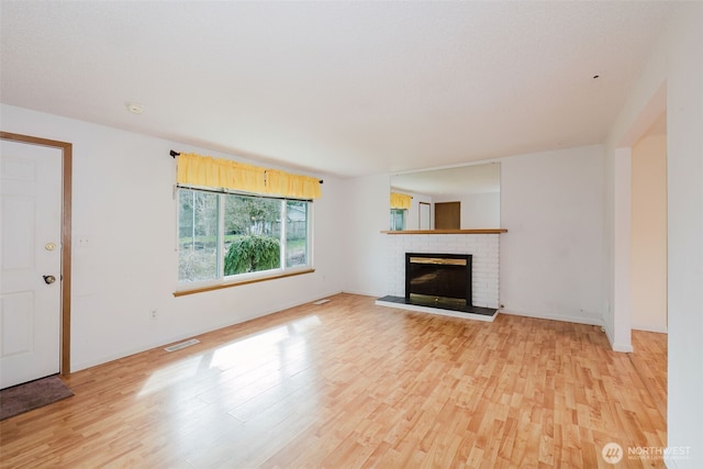 unfurnished living room featuring visible vents, baseboards, a brick fireplace, and light wood finished floors