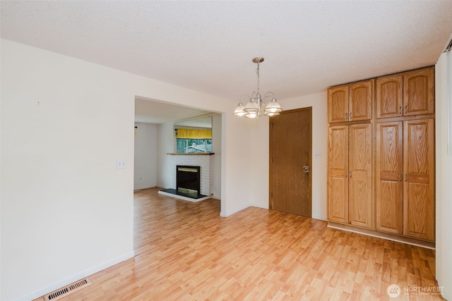 interior space featuring a brick fireplace, light wood-style floors, visible vents, and a chandelier