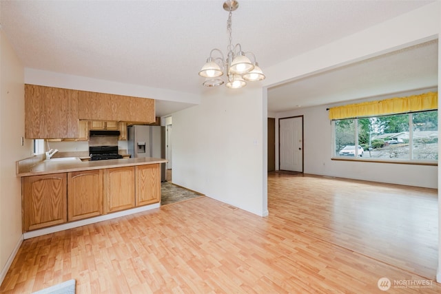 kitchen featuring light wood finished floors, black gas range, stainless steel fridge, a peninsula, and light countertops