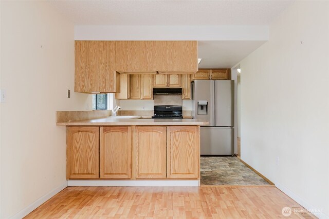 kitchen with black stove, stainless steel refrigerator with ice dispenser, under cabinet range hood, a peninsula, and light countertops