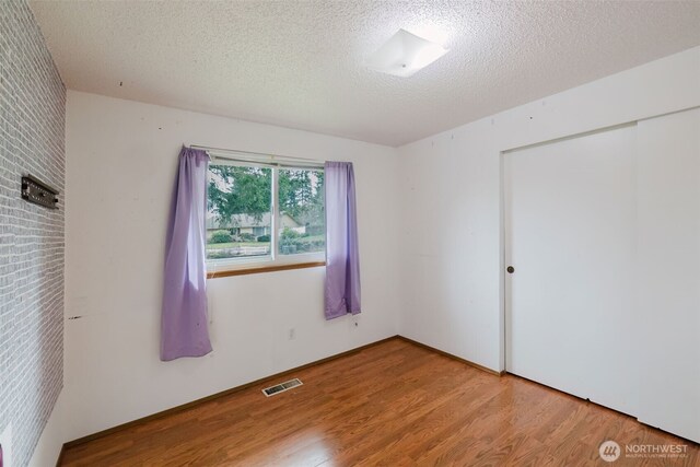 unfurnished bedroom with a closet, visible vents, a textured ceiling, and wood finished floors