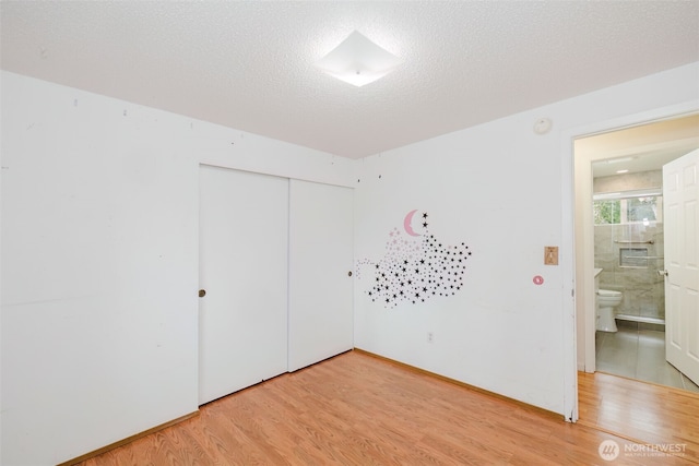 unfurnished bedroom featuring light wood-type flooring, baseboards, a textured ceiling, and a closet