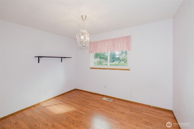 unfurnished room featuring visible vents, baseboards, light wood-style flooring, and a chandelier