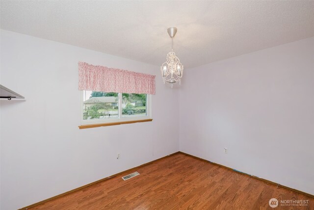 spare room featuring a notable chandelier, wood finished floors, visible vents, and a textured ceiling