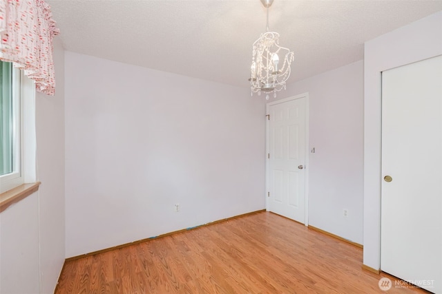 spare room with a chandelier, light wood-style flooring, a textured ceiling, and baseboards