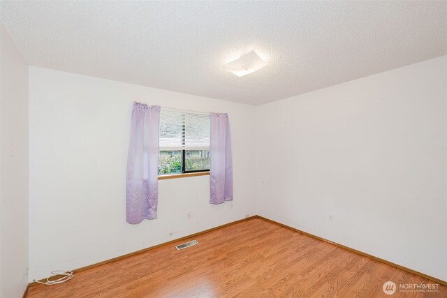 unfurnished room featuring visible vents, baseboards, a textured ceiling, and light wood-style flooring