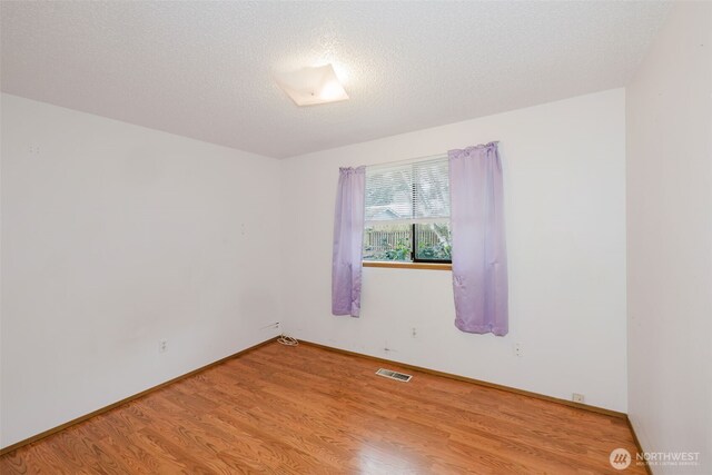 empty room with visible vents, baseboards, a textured ceiling, and light wood-style flooring