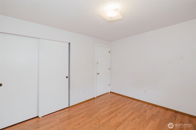 unfurnished bedroom featuring a closet, baseboards, a textured ceiling, and light wood-style floors