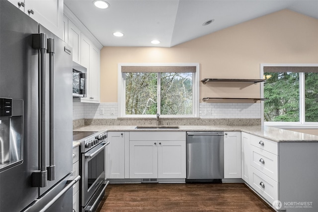 kitchen with a sink, dark wood finished floors, stainless steel appliances, white cabinets, and vaulted ceiling