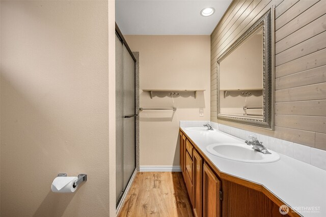 bathroom with double vanity, wood finished floors, a stall shower, and a sink