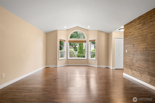 spare room featuring lofted ceiling, recessed lighting, wooden walls, baseboards, and dark wood-style flooring