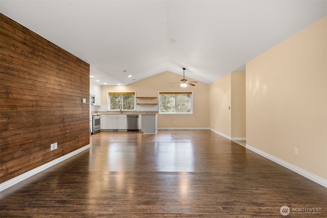 unfurnished living room featuring wooden walls, baseboards, ceiling fan, dark wood-type flooring, and vaulted ceiling