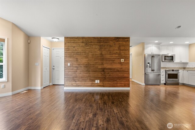 unfurnished living room with recessed lighting, wood walls, baseboards, and dark wood-style flooring