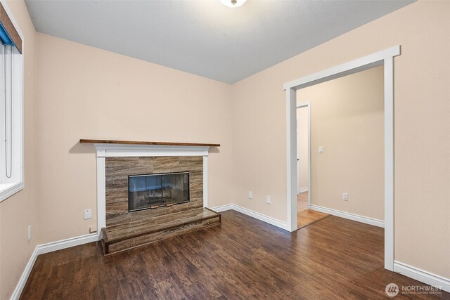 unfurnished living room with a tiled fireplace, baseboards, and wood finished floors