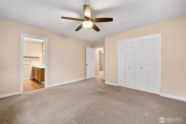 unfurnished bedroom with a closet, light colored carpet, ensuite bathroom, and baseboards