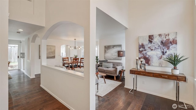 corridor with a towering ceiling, baseboards, arched walkways, and dark wood-style flooring