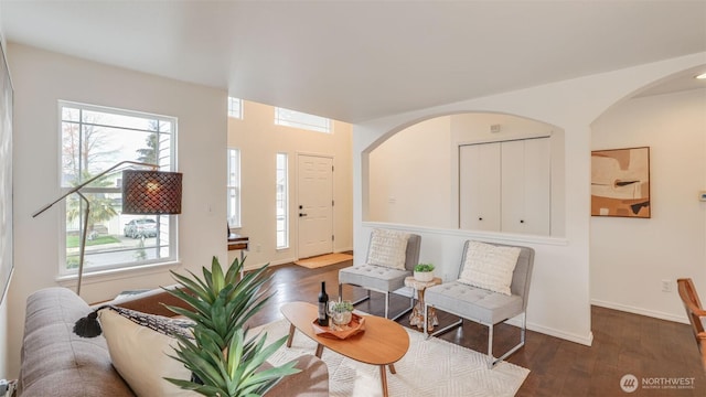 living area with arched walkways, baseboards, and wood finished floors