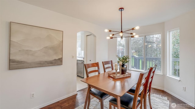 dining space with wood finished floors, a healthy amount of sunlight, arched walkways, and a chandelier